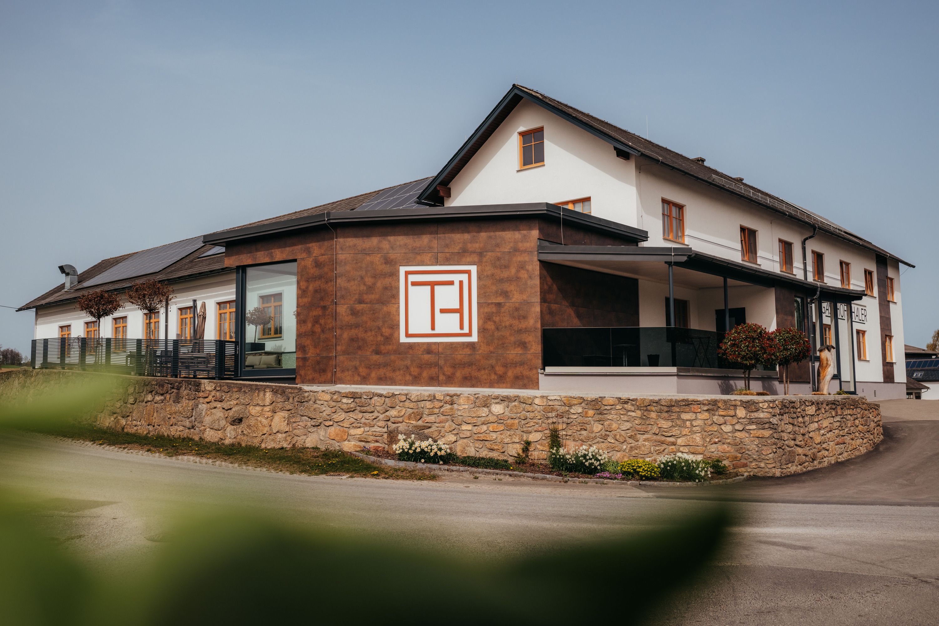 A "Gasthof Thaler" feliratú modern épületet kőfal és növények veszik körül.