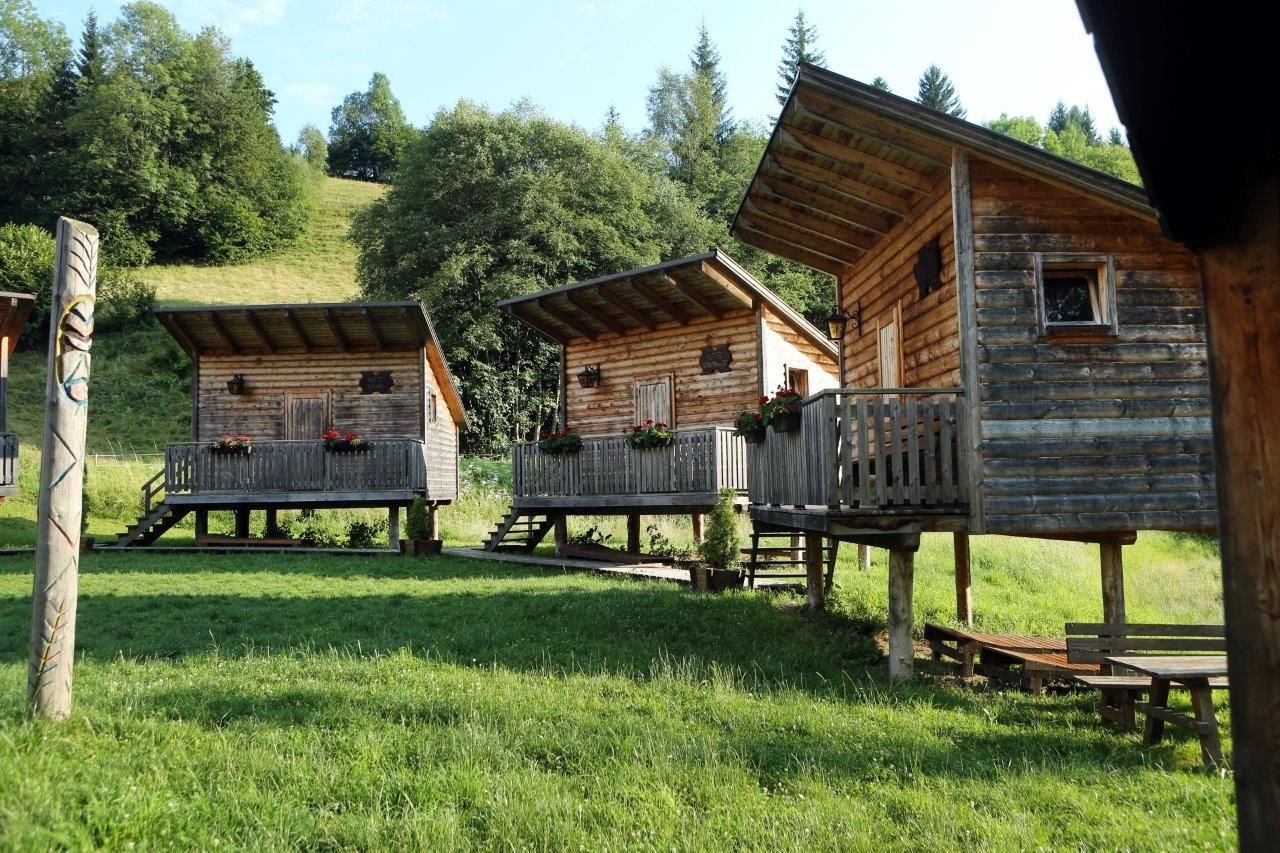 Három cölöpökön álló faházikó verandával egy zöld, erdős területen.