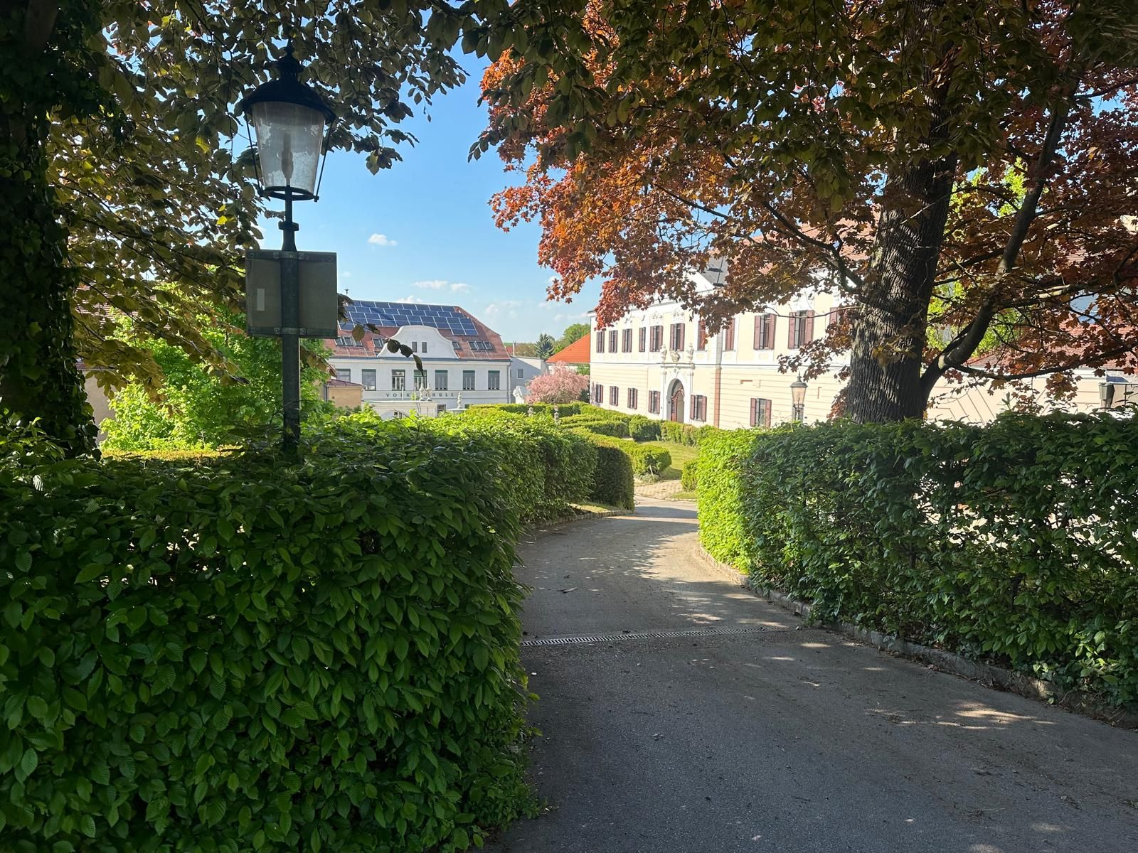 Egy nagyrußbachi kastély látképe, fákkal és sövénnyel körülvéve, előtérben egy lámpás.
