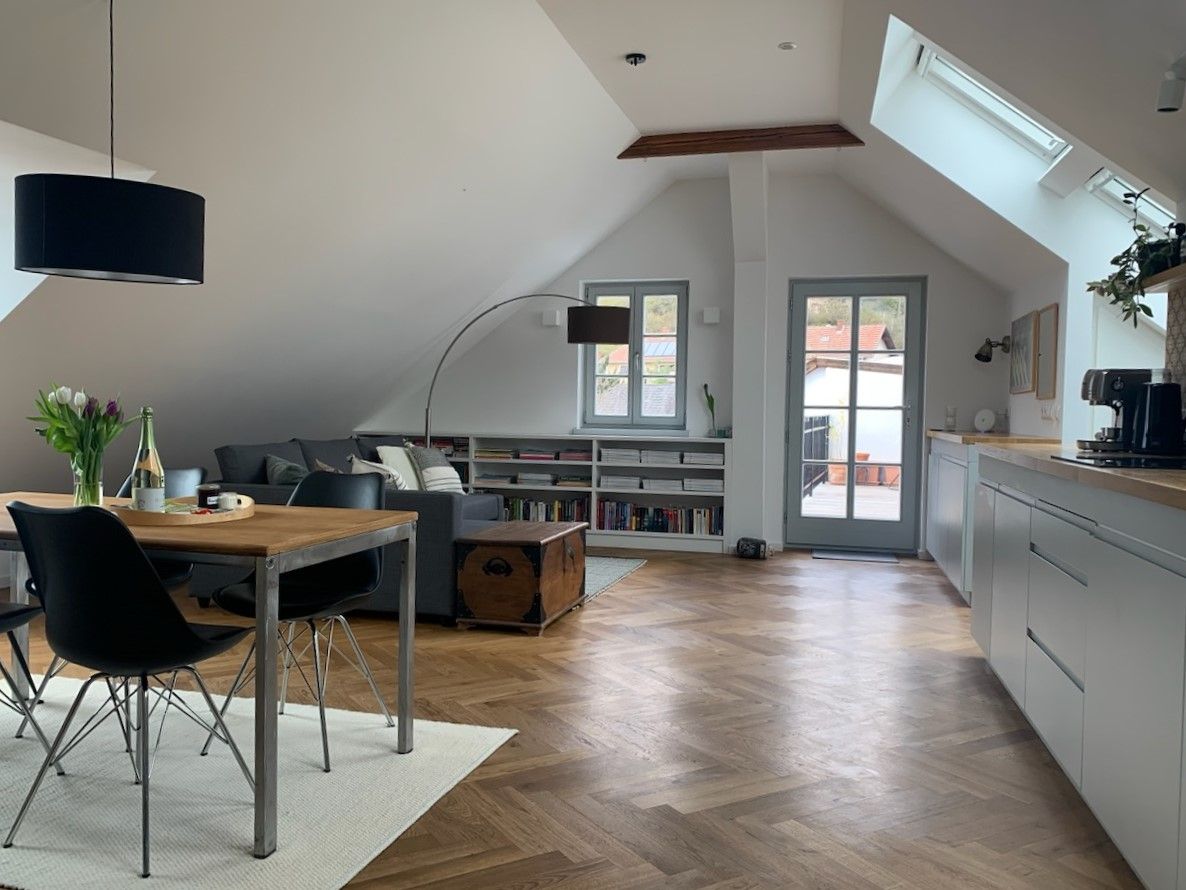 Modern tetőtéri lakás fapadlóval, étkezőasztallal, kanapéval és erkélykapcsolattal.