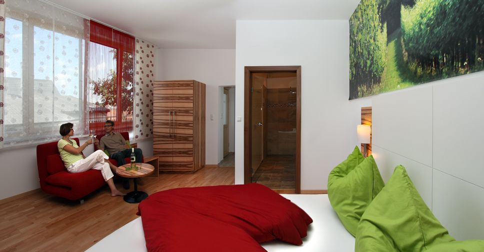Modern vendégszoba piros kanapéval, zöld-piros ággyal és nagy ablakkal.
