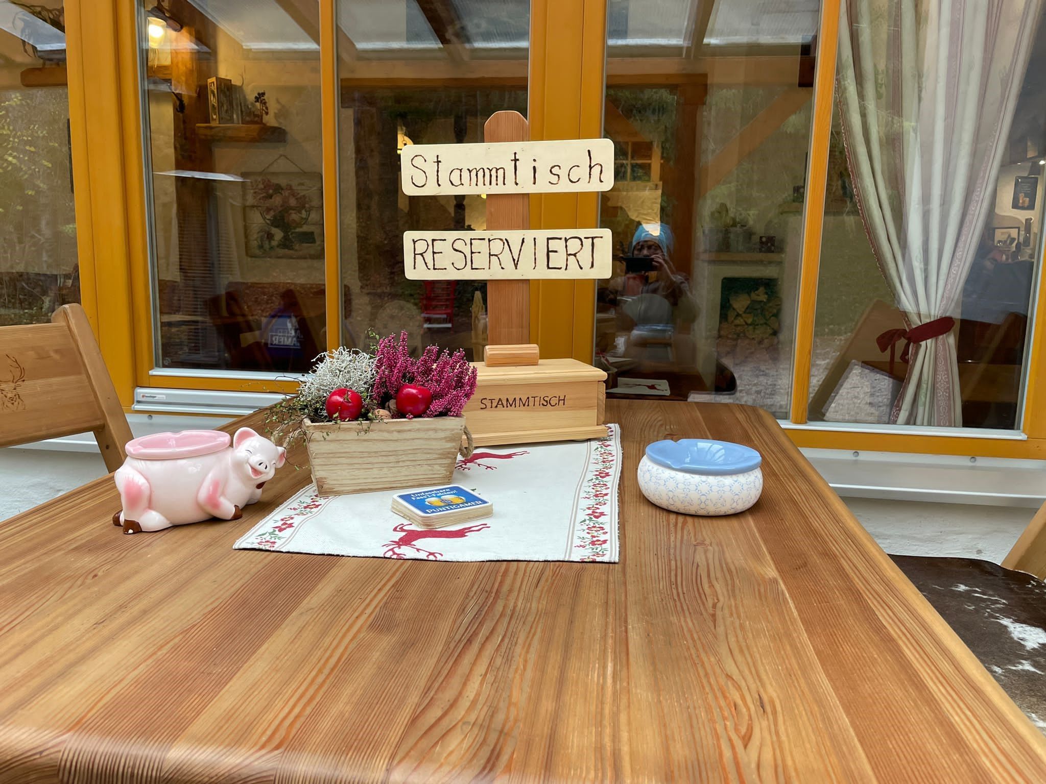 Egy rusztikus asztal "Stammtisch Reserviert" felirattal, dekorációval és hamutartóval.