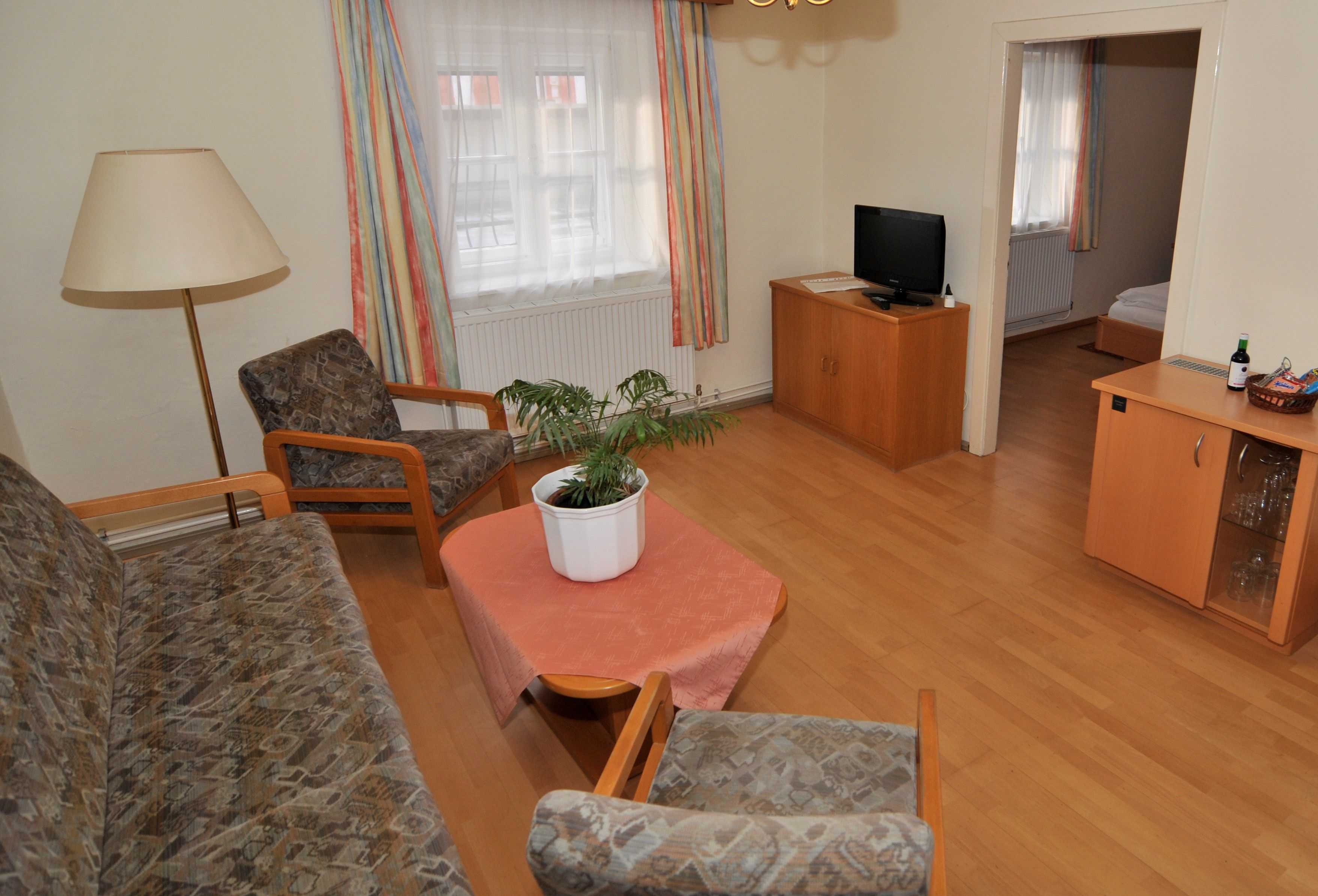 Nappali kanapéval, két fotel, asztal növényekkel, TV és hozzáférés a hálószobához.