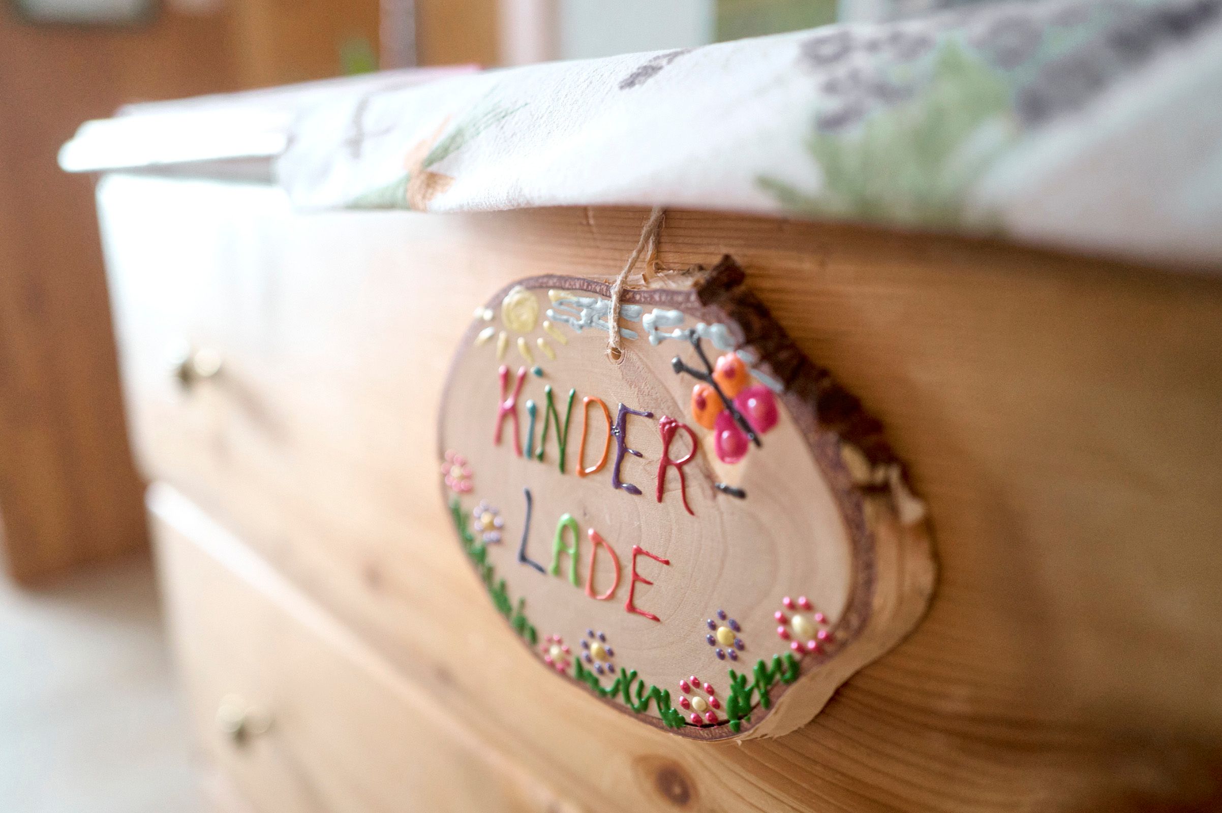 Közelkép egy komódon lévő "Kinderlade" feliratú fatábláról.