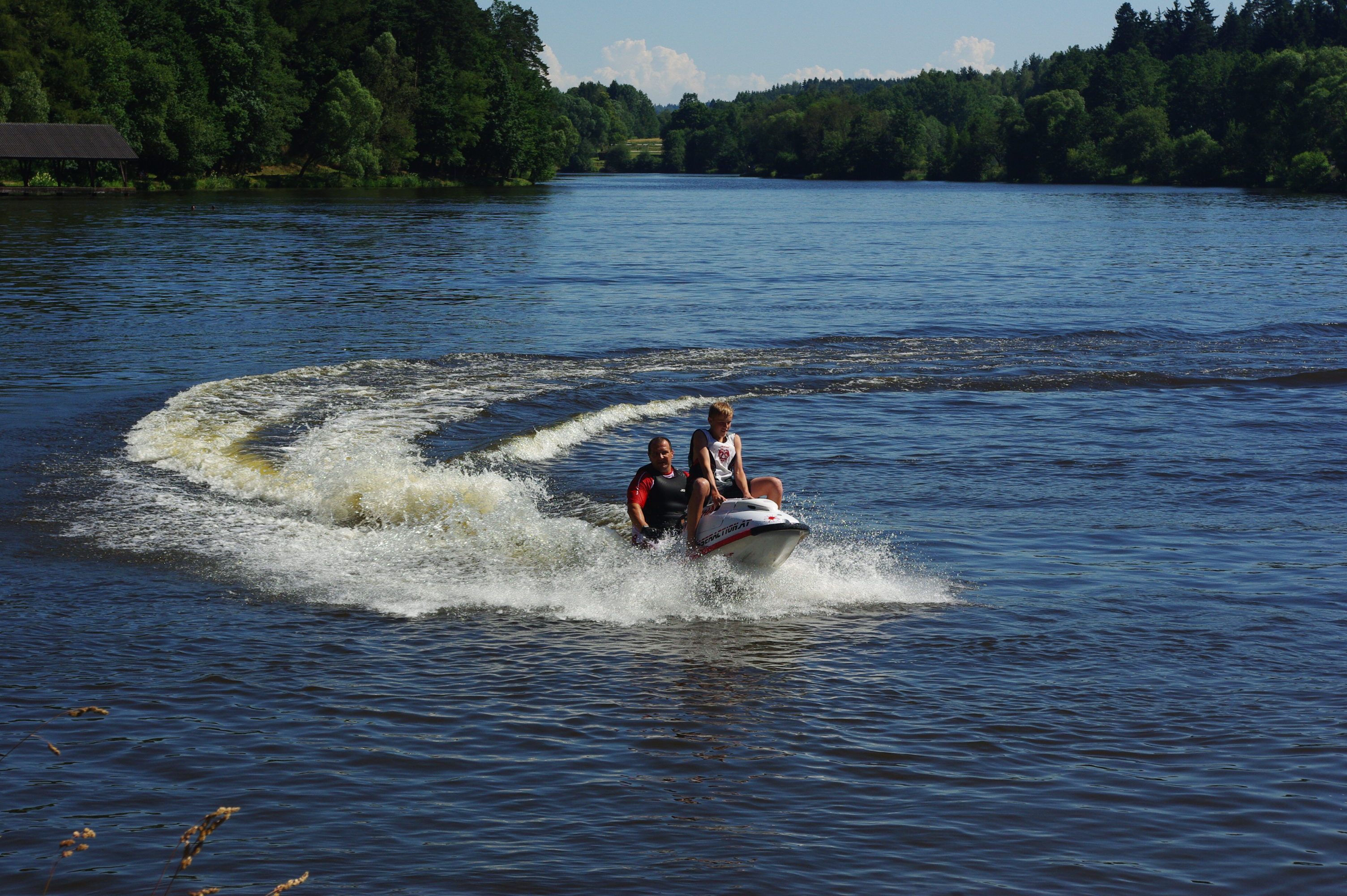 Két ember jet-skivel szeli át a fákkal körülvett tavat.