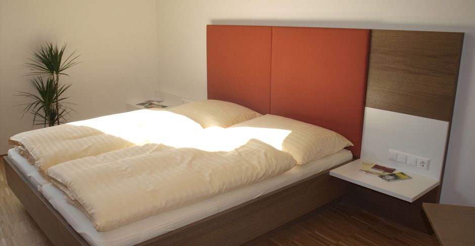 Modern vendégszoba franciaággyal, piros fejtámlával és növényekkel.