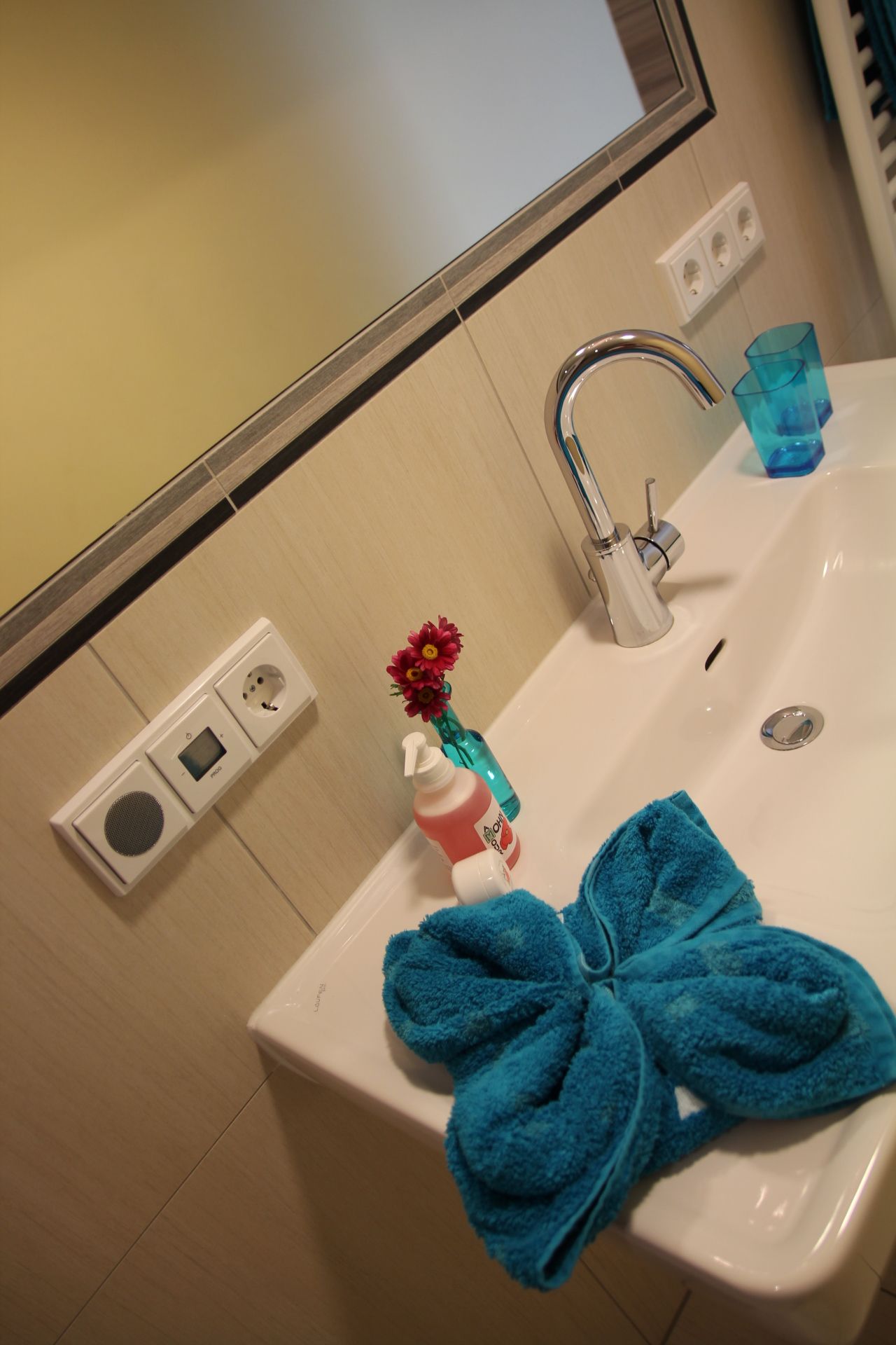 Mosdókagyló kék törülközővel, szappanadagolóval és virágos vázával.