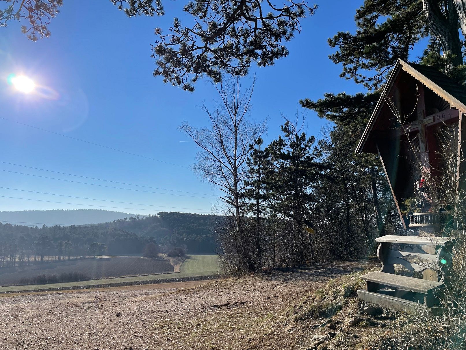 Tájkép turistaházsal és fákkal a napsütésben.