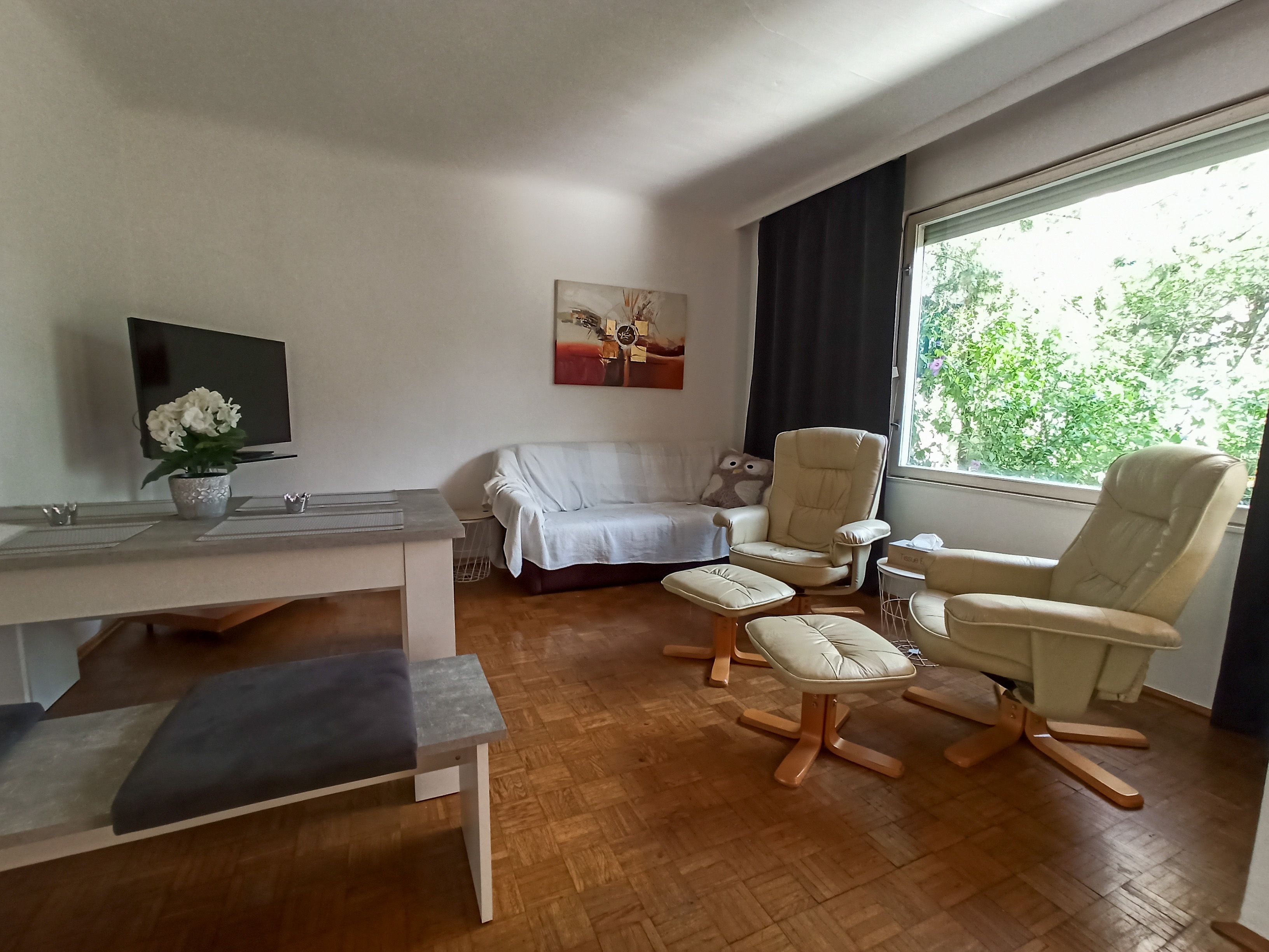 Nappali kanapéval, két fotel, asztal és nagy ablak.