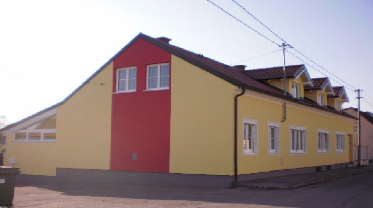 Egy sárga-piros színű, több ablakkal és nyeregtetővel rendelkező épület külső nézete.