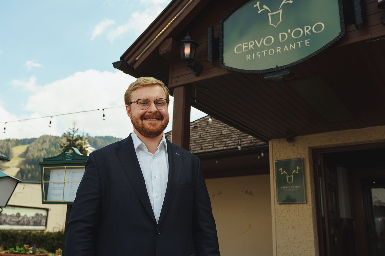 Egy öltönyös férfi áll mosolyogva a Cervo D'Oro étterem előtt.