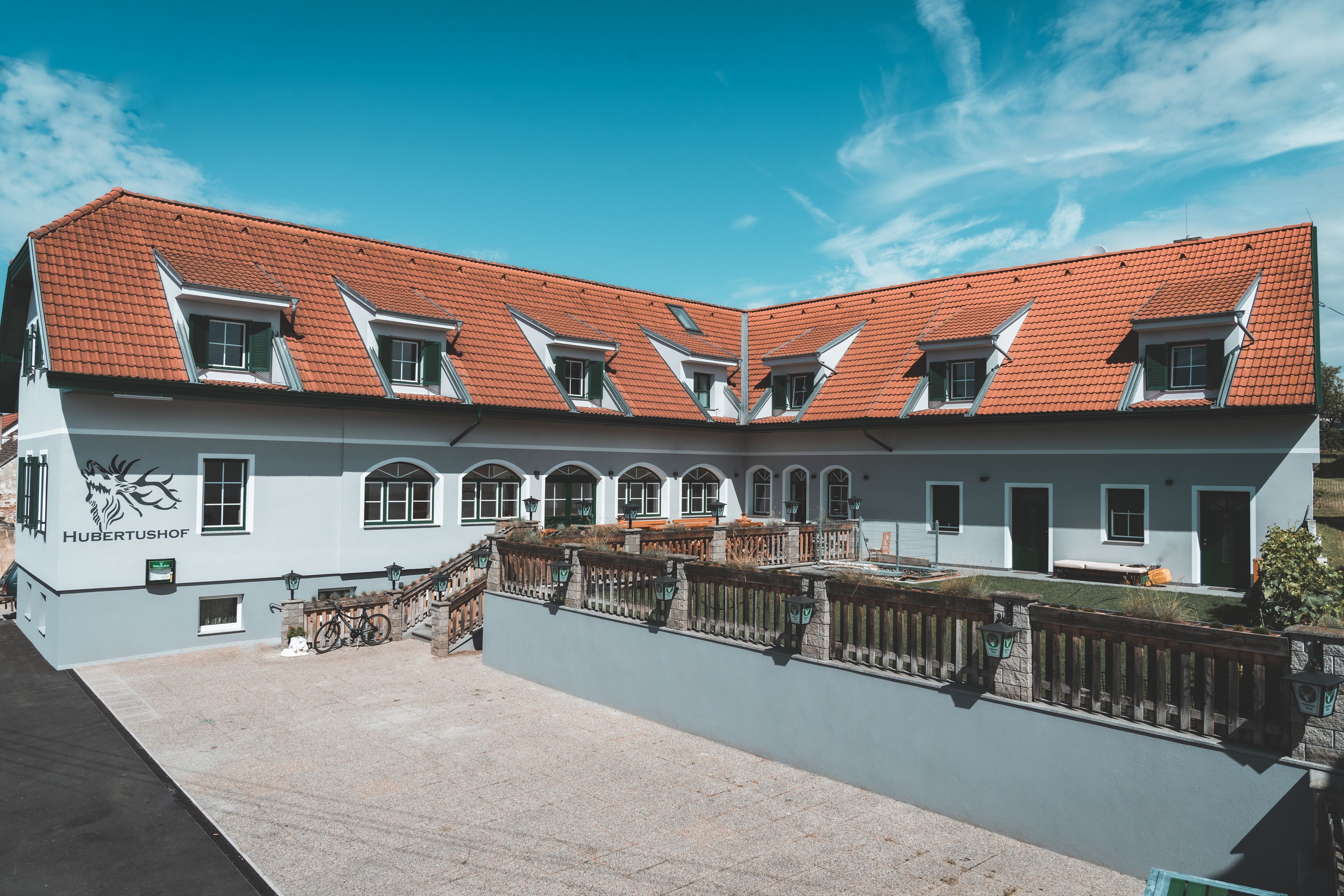 Vörös tetőcseréppel és több tetőablakkal ellátott épület, "Hubertushof" felirattal.