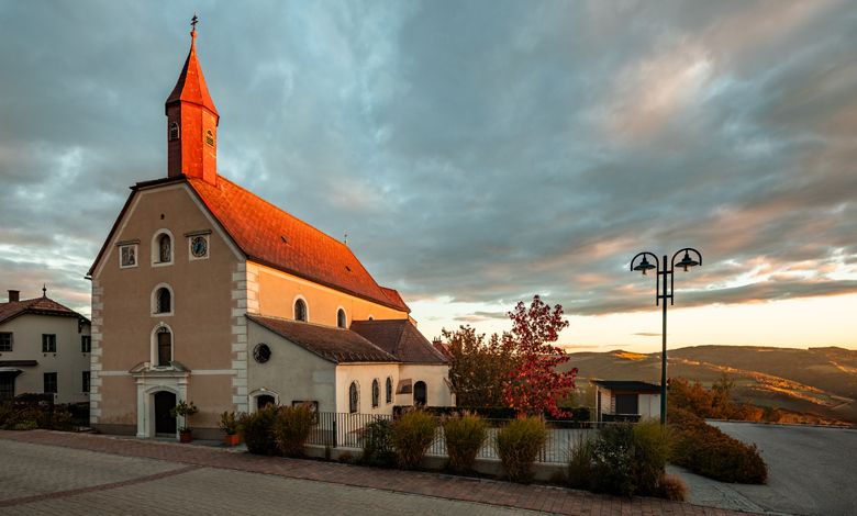A Szent Korona am Wechsel zarándoktemplom naplementekor, drámai égbolt mellett.