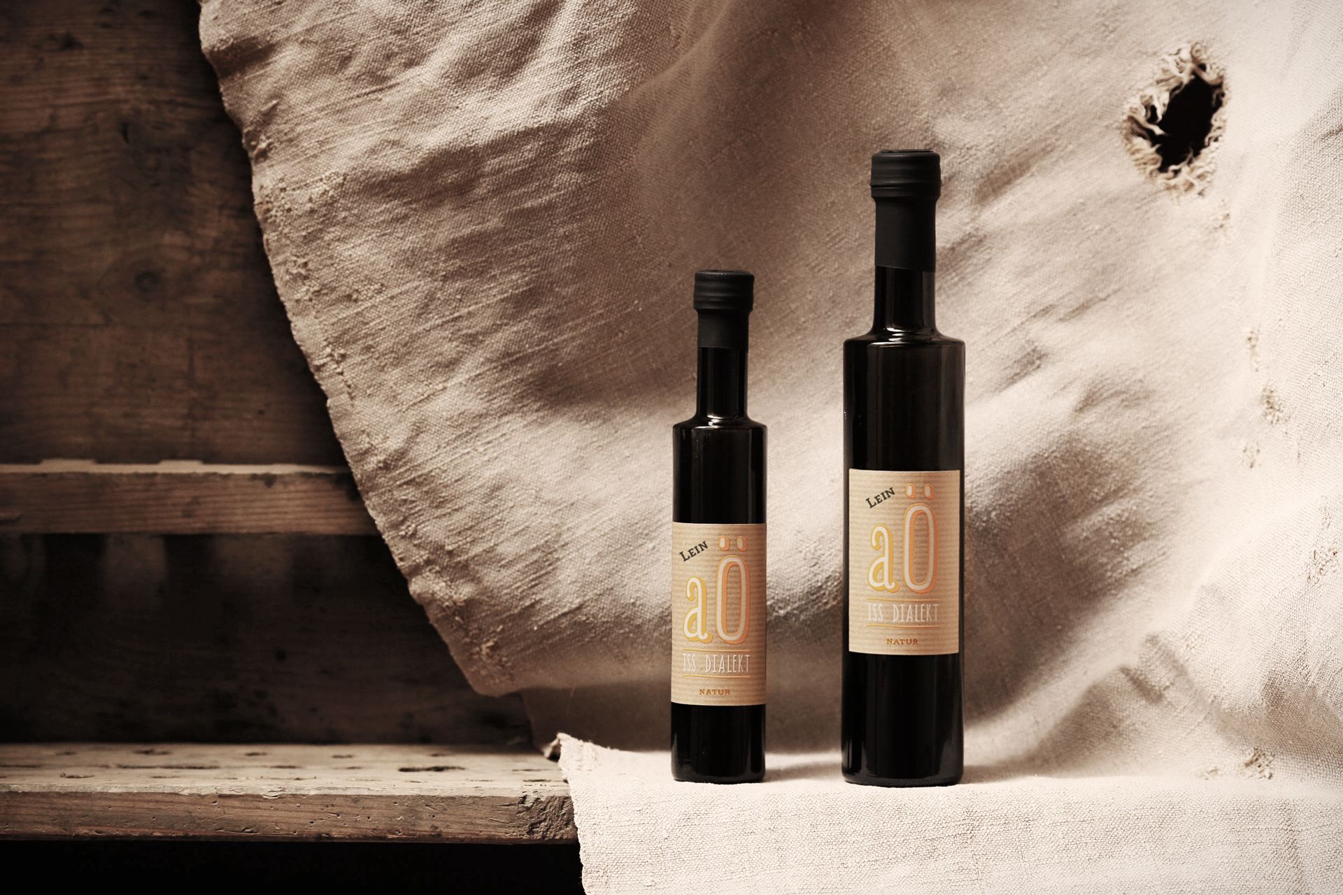 Két üveg lenolajos palack rusztikus háttér előtt.