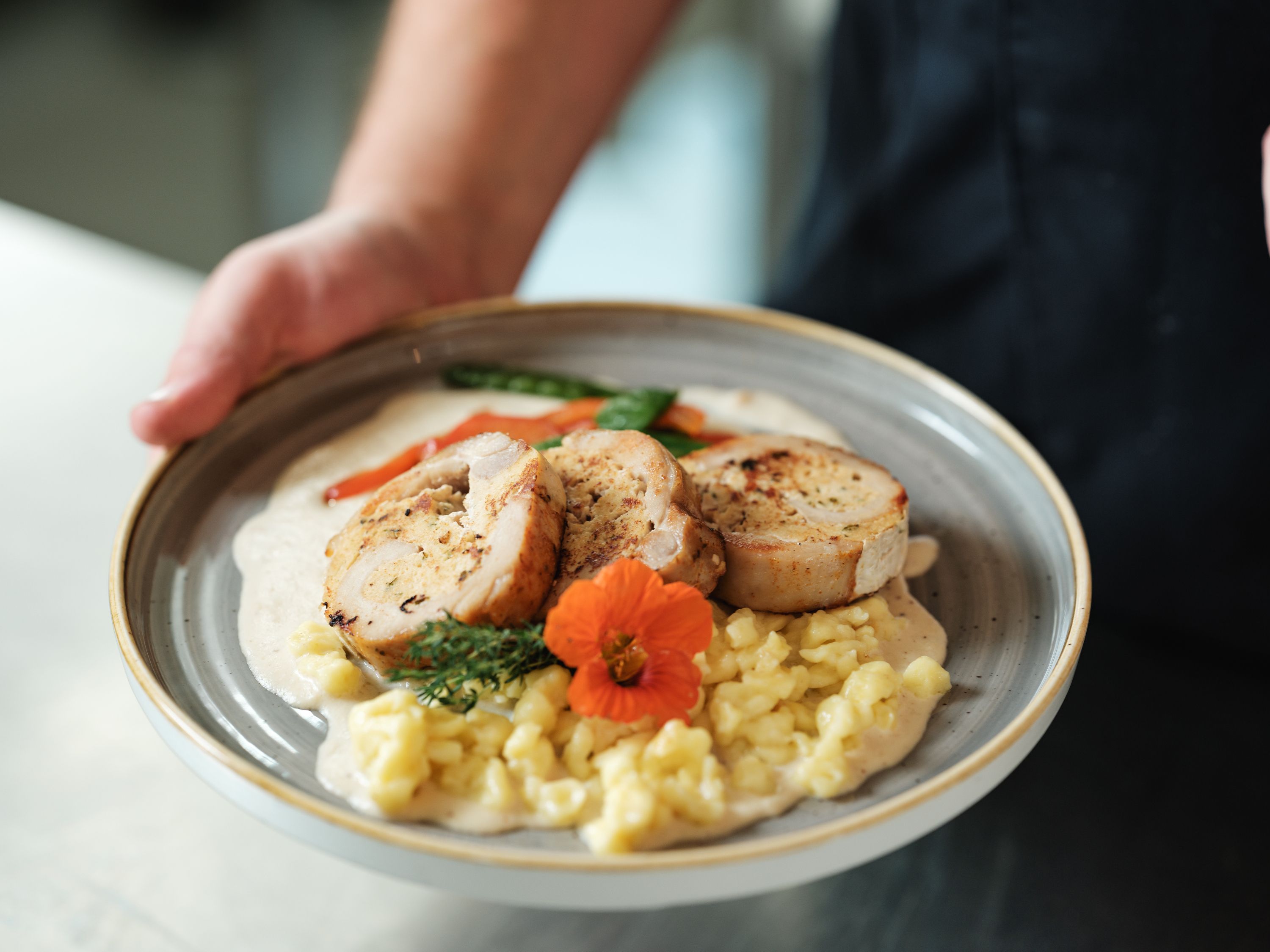 Egy tányér töltött hússal, spagettivel, zöldségekkel és virággal díszítve.