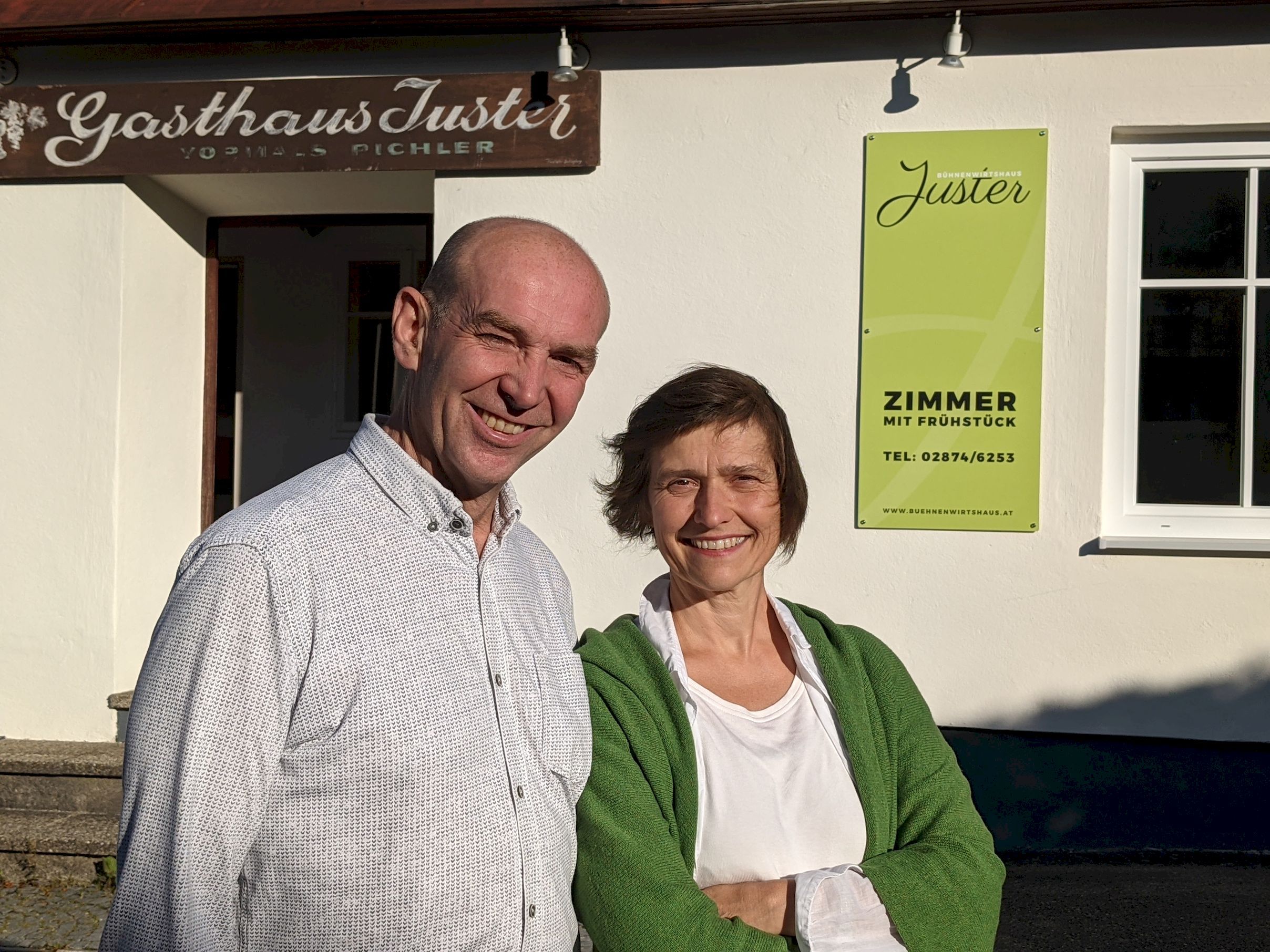 Egy férfi és egy nő áll mosolyogva a Jüster vendéglő előtt. A háttérben tábla: "Szoba reggelivel".