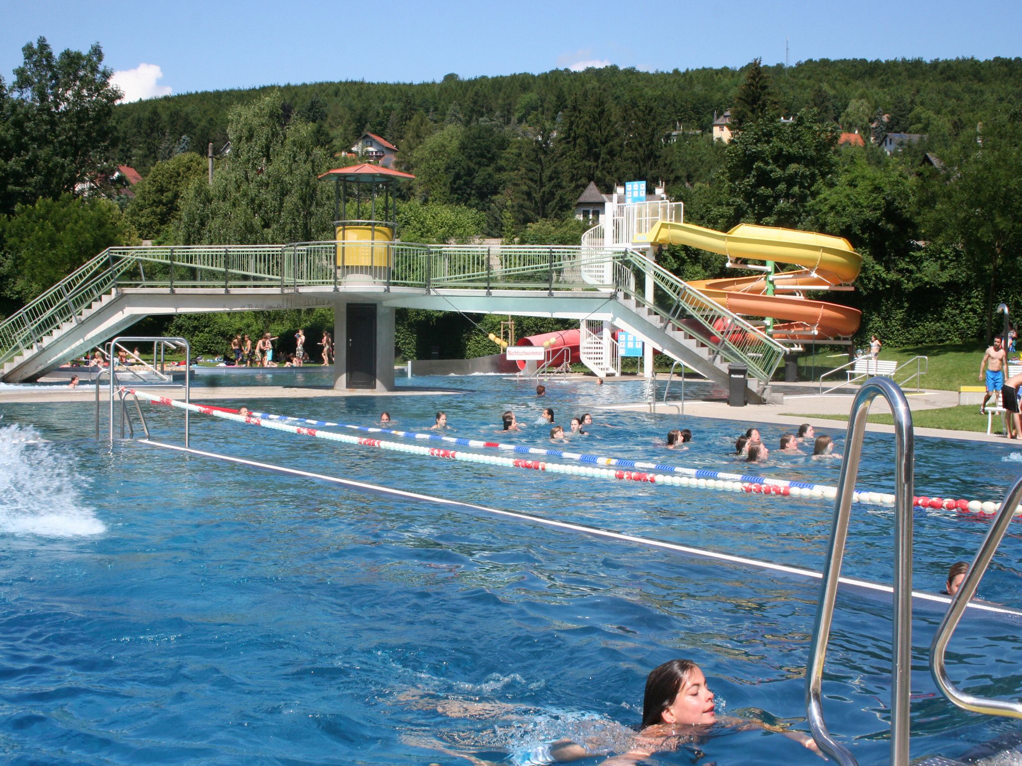 Kültéri medence úszókkal, csúszdával és híddal a Wienerwaldbad Purkersdorfban.