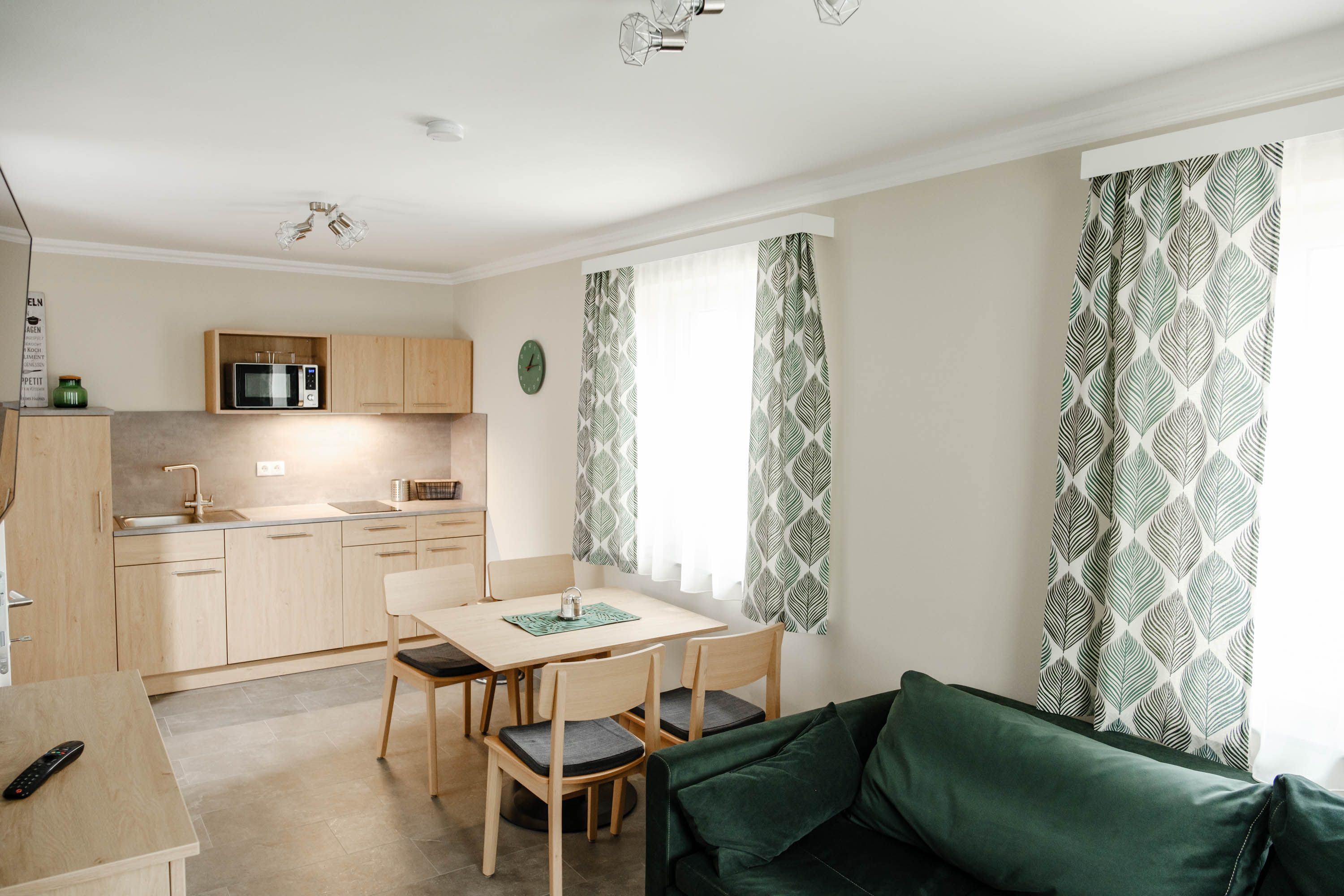 Modern konyha fabútorokkal, étkezőasztallal, zöld függönyökkel és kanapéval.