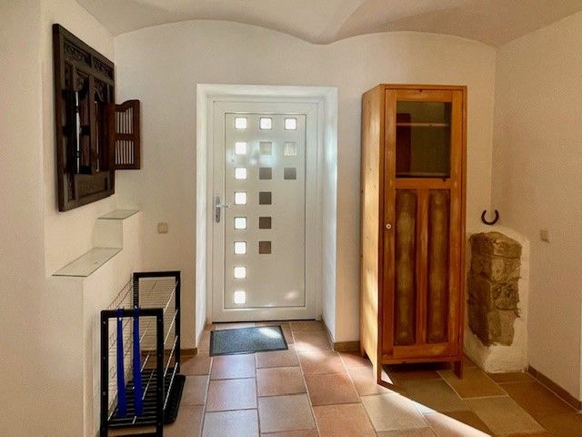 Bejárati rész fehér ajtóval, fa szekrénnyel és csempézett padlóval.