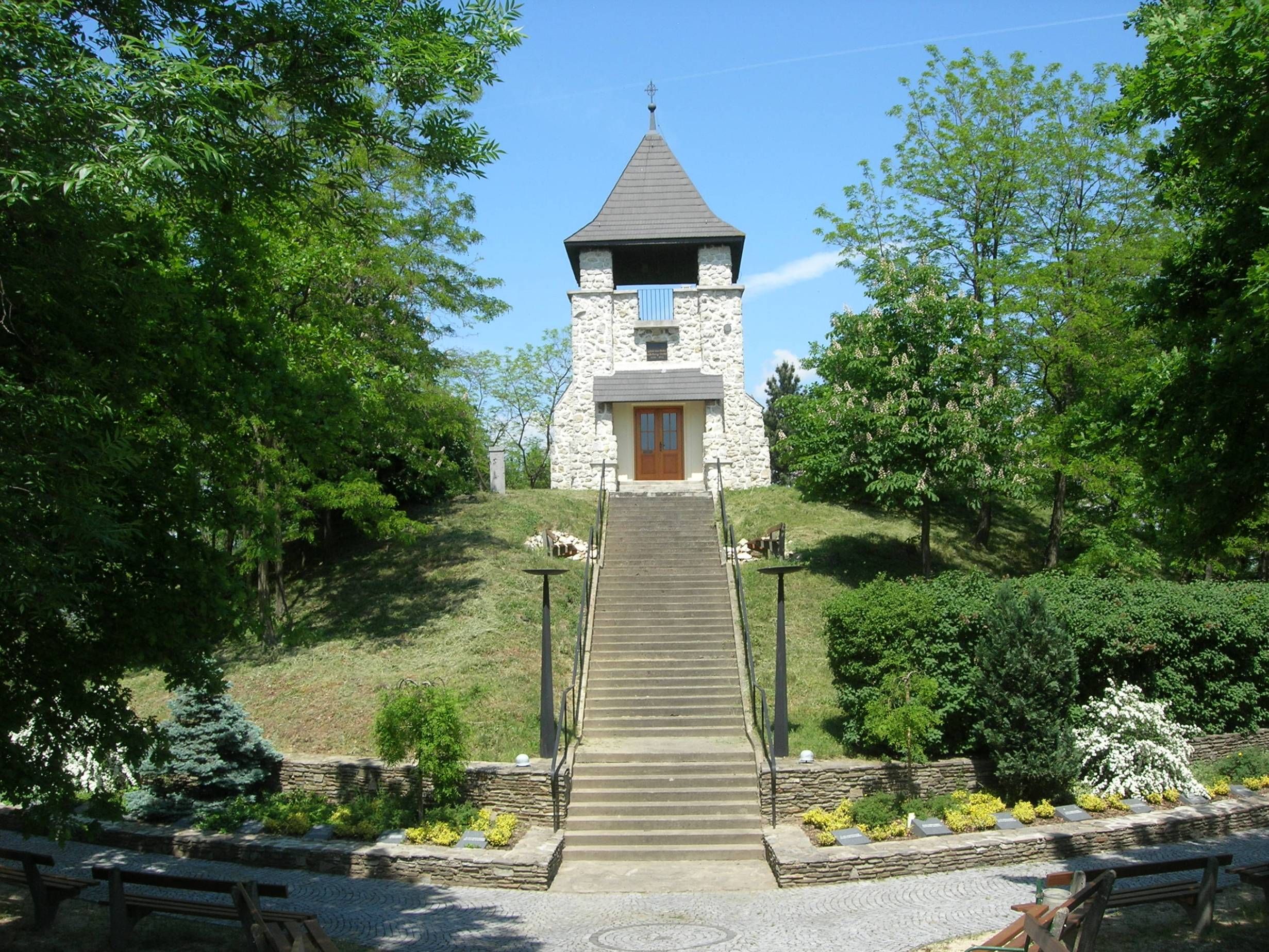 Kőtorony egy dombon, lépcsőkkel és zöld környezettel.