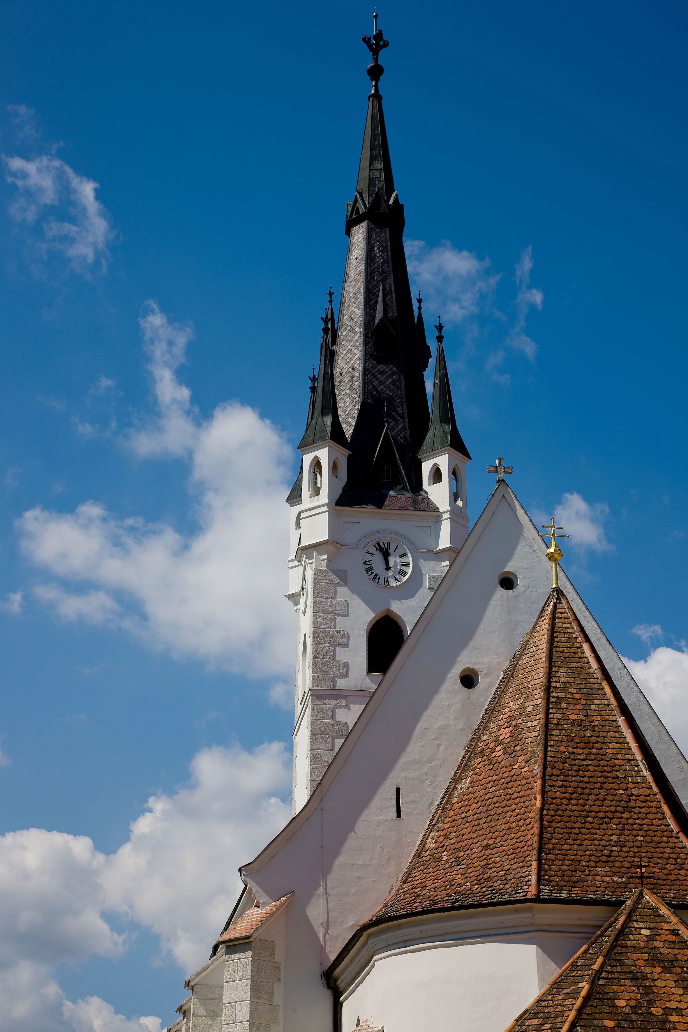 Templomtorony órával és csúcsos tetővel a kék égbolton.