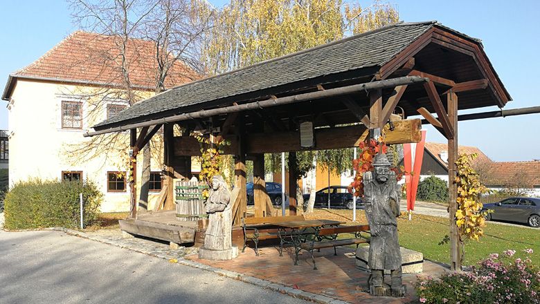Történelmi fa prés, fa figurákkal a Droßban, őszi növényzettel körülvéve.