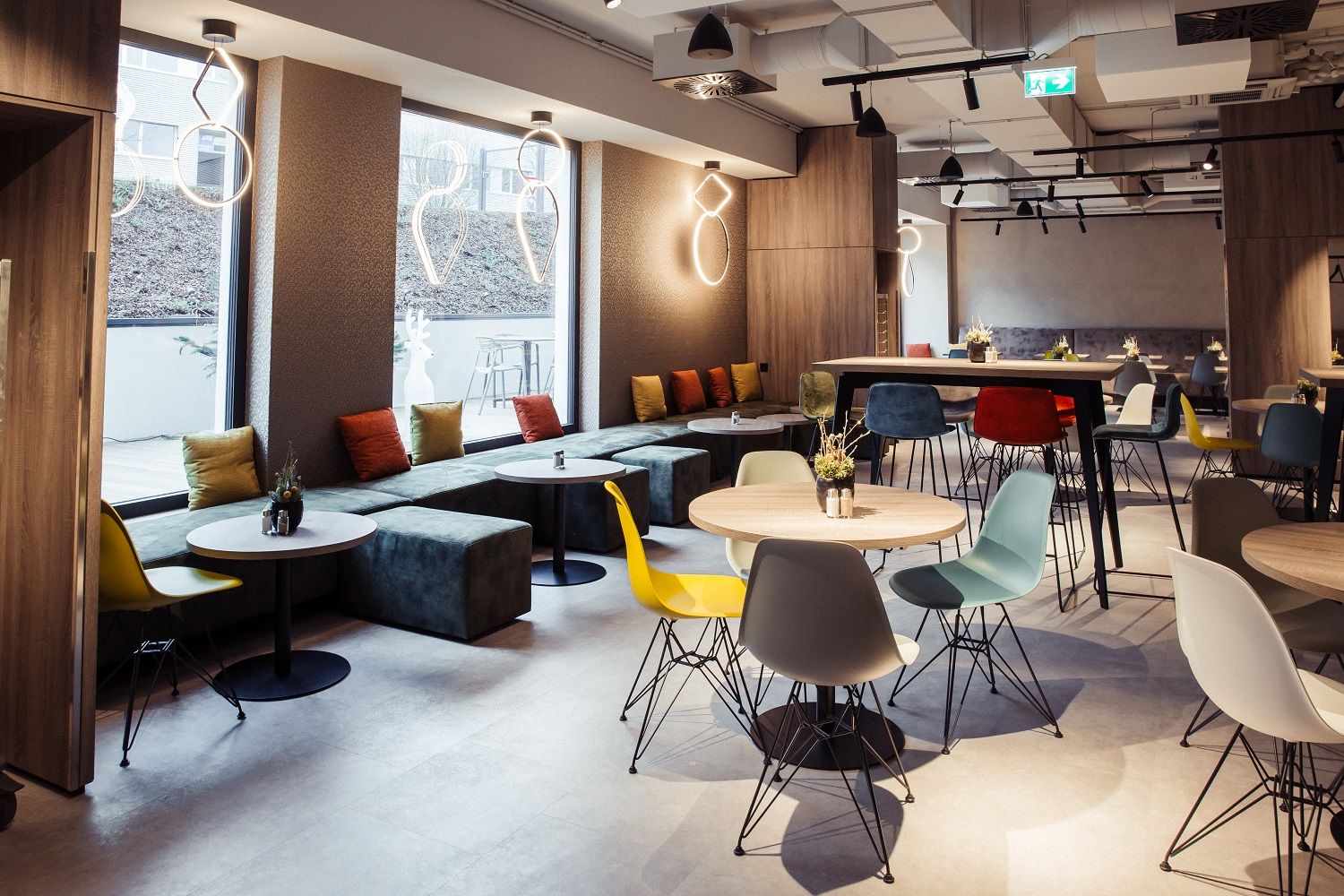 Modern szállodaétterem színes székekkel és asztalokkal, nagy ablakokkal és stílusos világítással.