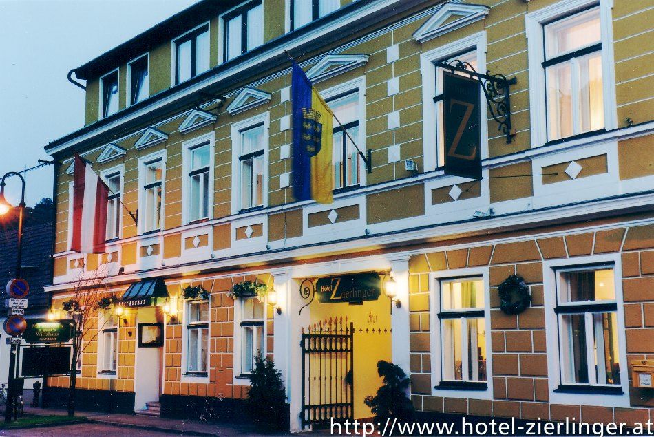 A Hotel Zierlinger külső nézete sárga homlokzattal és zászlókkal.