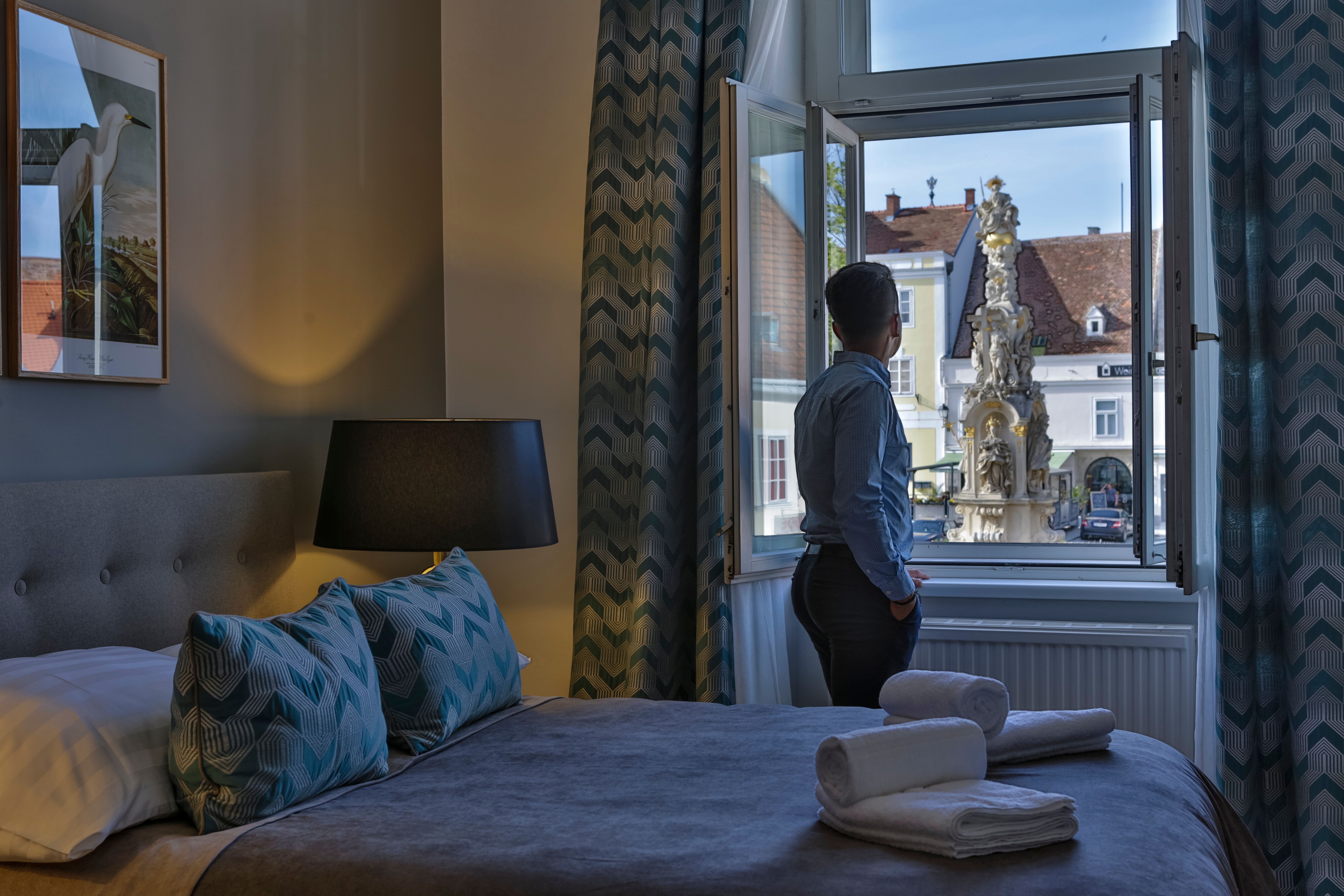 Egy személy egy szállodai szoba ablakánál áll, és a kinti szökőkutat nézi.