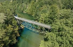 Eine malerische Brücke schwingt sich über das glitzernde Wasser, umgeben von üppigem Grün und majestätischen Bergen. Radfahrer genießen die frische Luft und die atemberaubende Aussicht auf die Ybbstaler Alpen, während sie die Ruhe der Natur erleben.