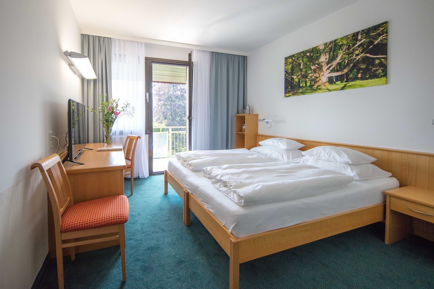 Hotelszoba franciaággyal, íróasztallal, székkel és erkéllyel.
