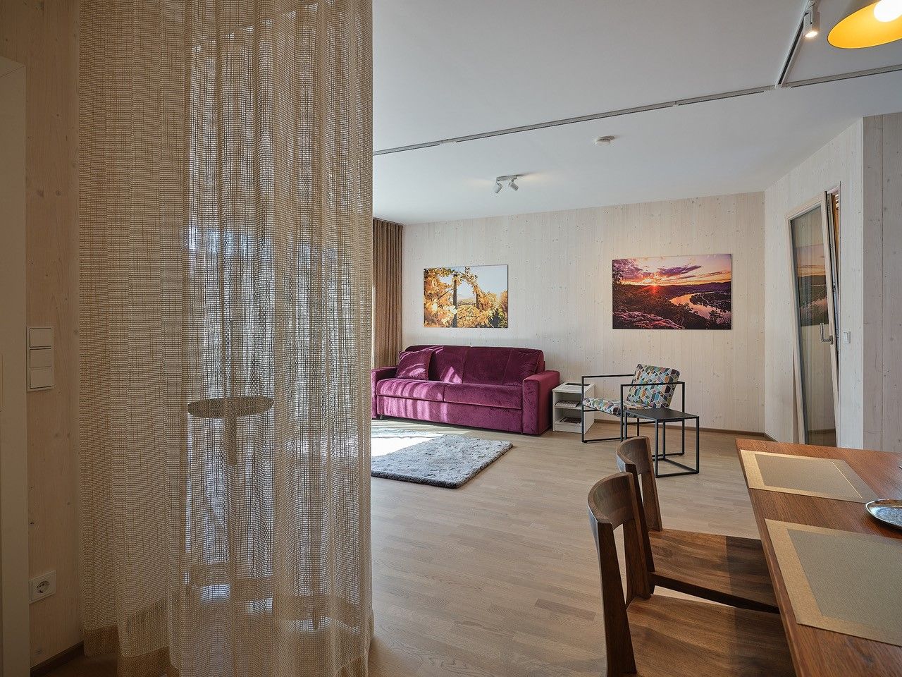 Nappali lila kanapéval, fa asztallal és székekkel, függönnyel és falfestményekkel.