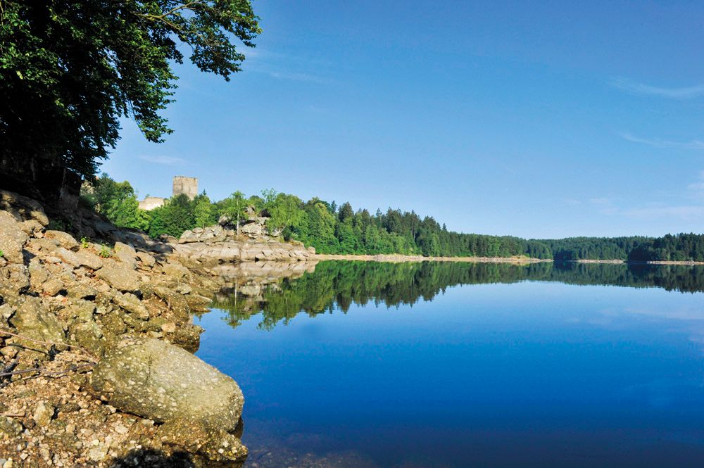 Kampsee Ottenstein nyugodt vízzel, erdős parttal és egy kastéllyal a háttérben.