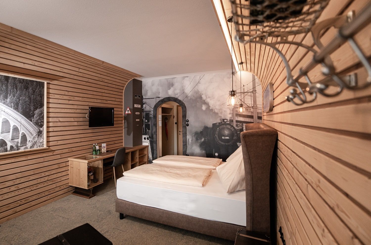 Hotelszoba fából készült falakkal, franciaággyal és egy nagy gőzmozdonyt ábrázoló freskóval.