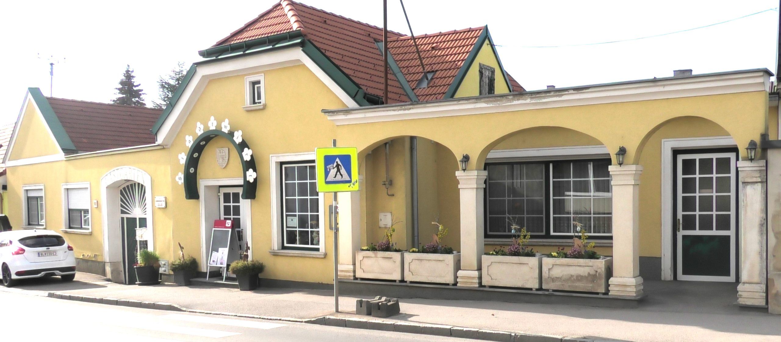 Külső nézet egy sárga árkádos épületről, piros tetővel.