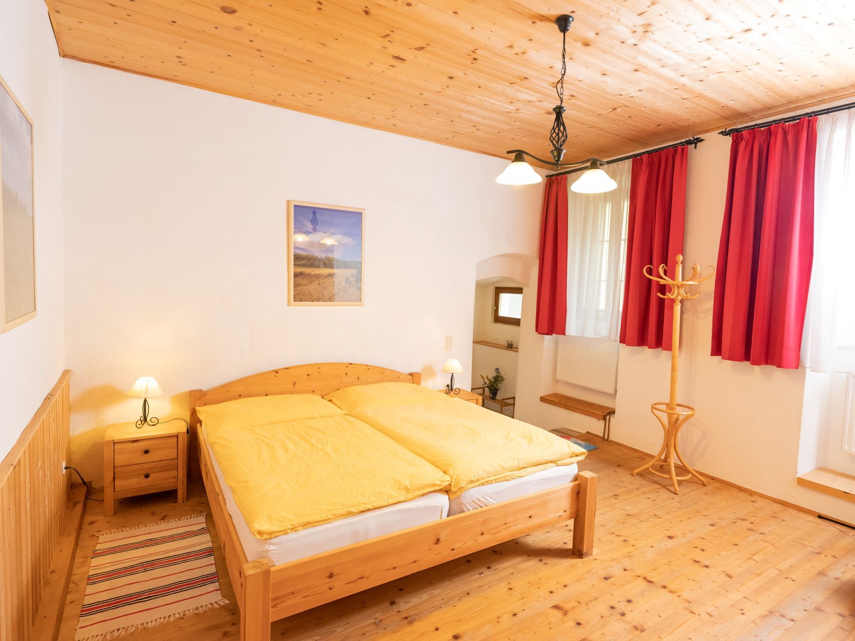 Hangulatos hálószoba fabútorokkal, sárga ágyneművel és piros függönyökkel.