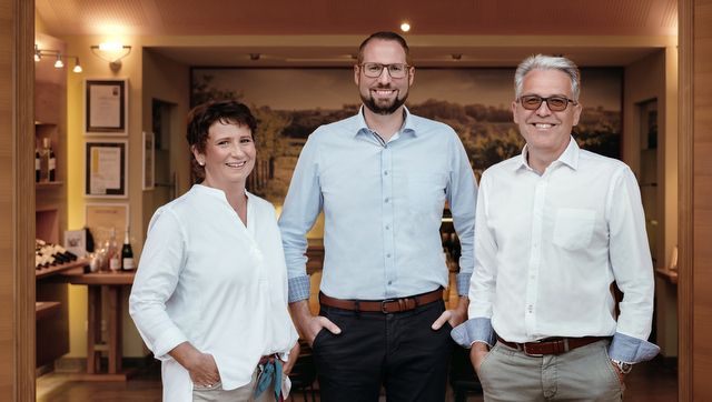 Három ember egy szobában, a háttérben borosüvegekkel.