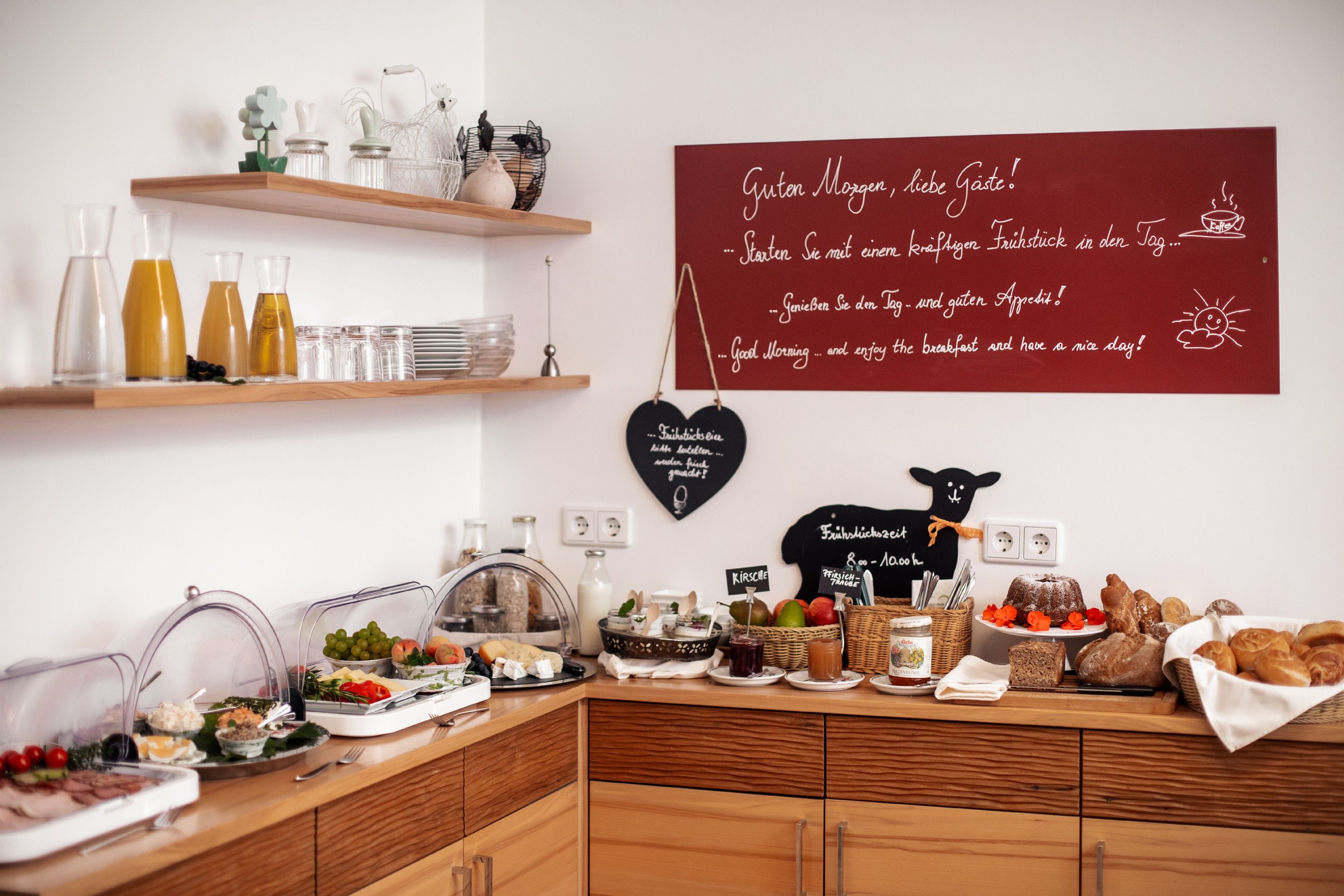 Büféreggeli gyümölcslevekkel, kenyérrel, felvágottakkal és gyümölcsökkel egy hangulatos teremben.