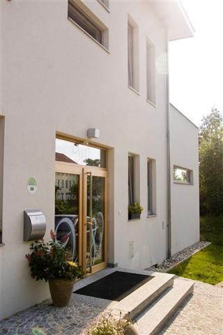 Egy modern épület bejárata üveg- és faajtóval, virágokkal egy cserépben és lépcsőkkel.