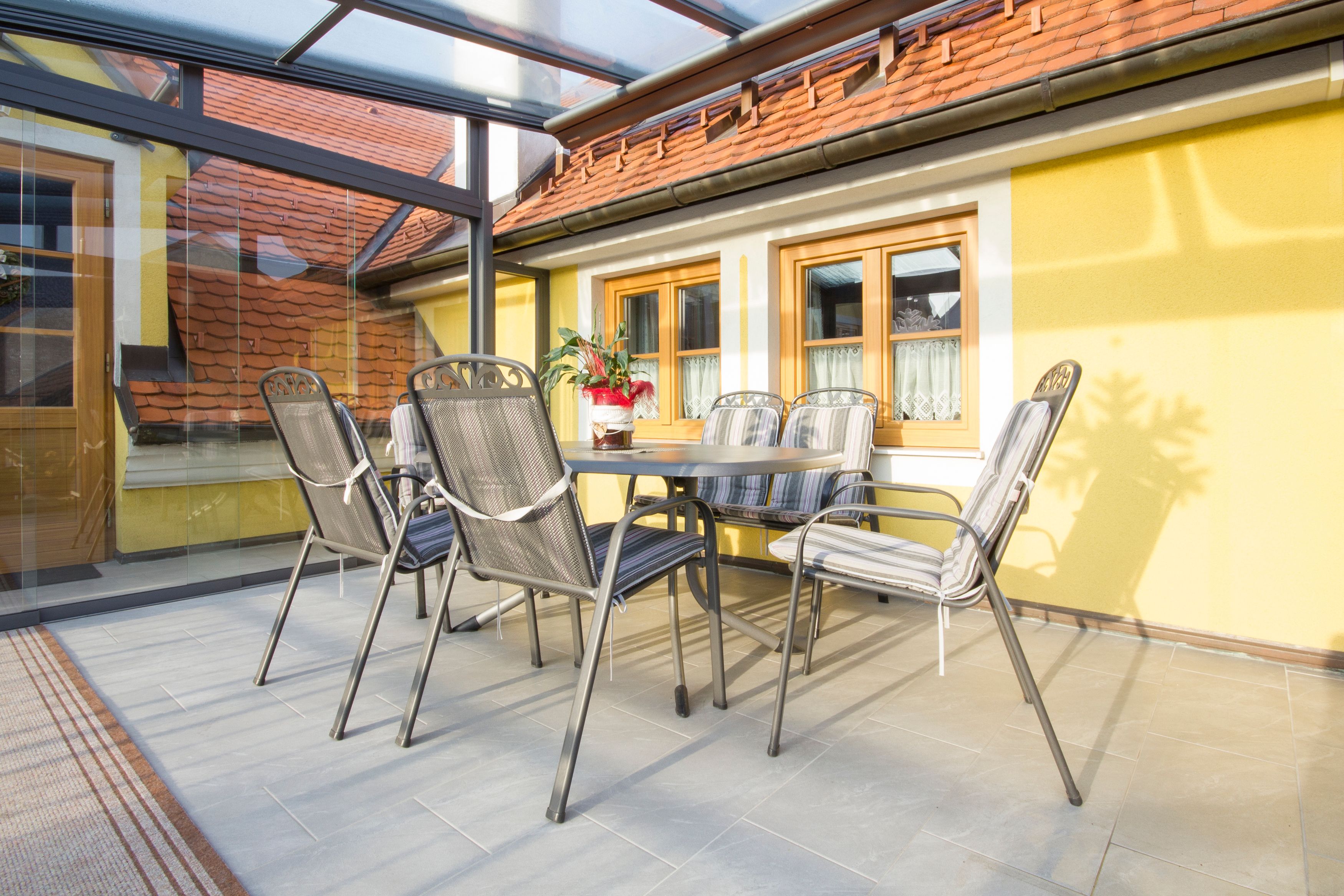 Télikert asztallal és székekkel, sárga falakkal, üvegtetővel.