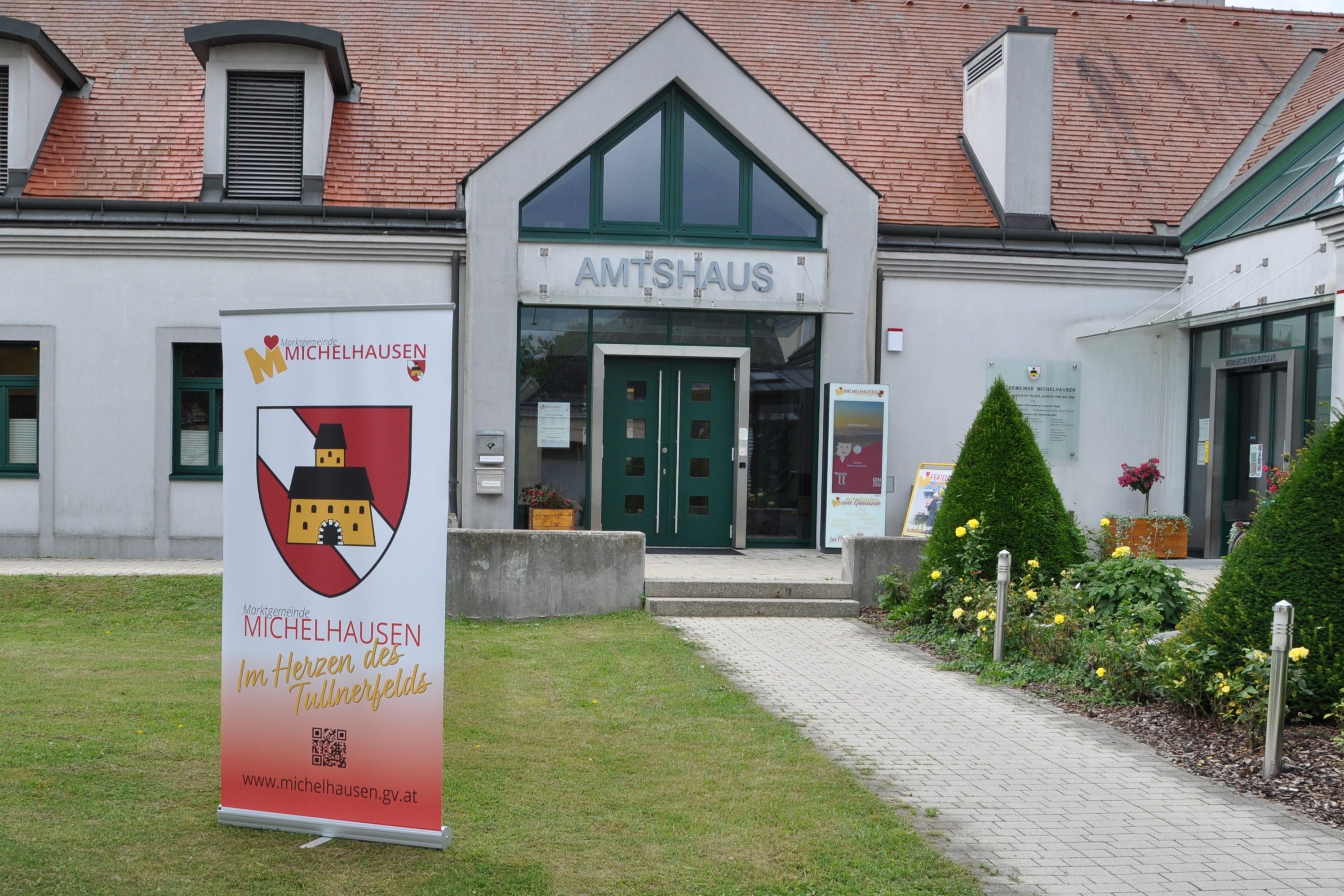 Az Amtshaus Michelhausen bejárata reklámszalaggal és gondozott kerttel.