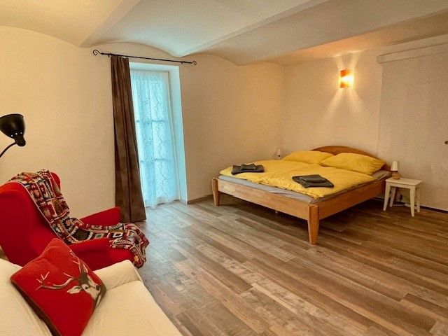 Hangulatos hálószoba fapadlóval, franciaággyal, piros fotel és függönyös ablak.