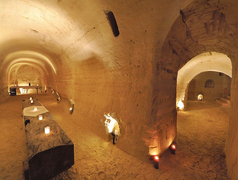 Földalatti homokkő pince gyertyafénnyel és rusztikus asztalokkal.