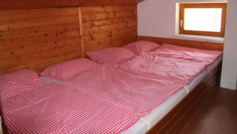 Három ágy, piros-fehér kockás paplanhuzattal egy fapadlós szobában.