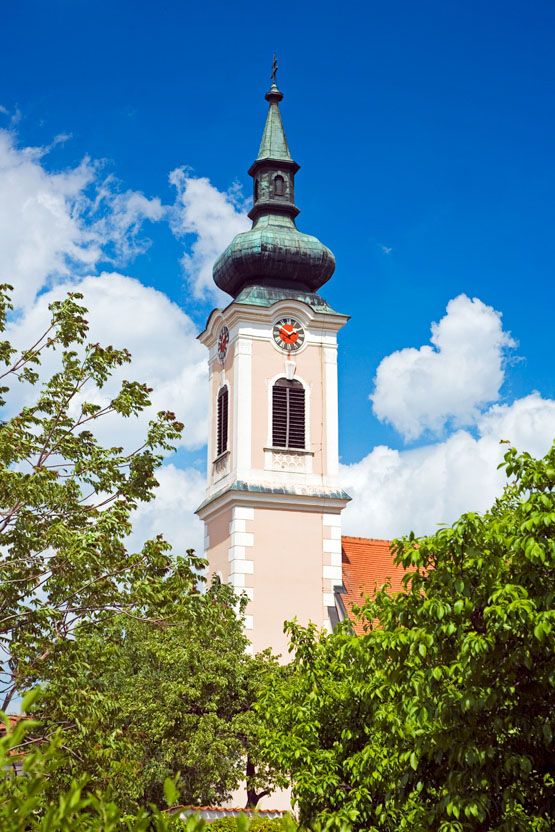 Templom tornya órával és zöld tetővel a kék ég előtt.