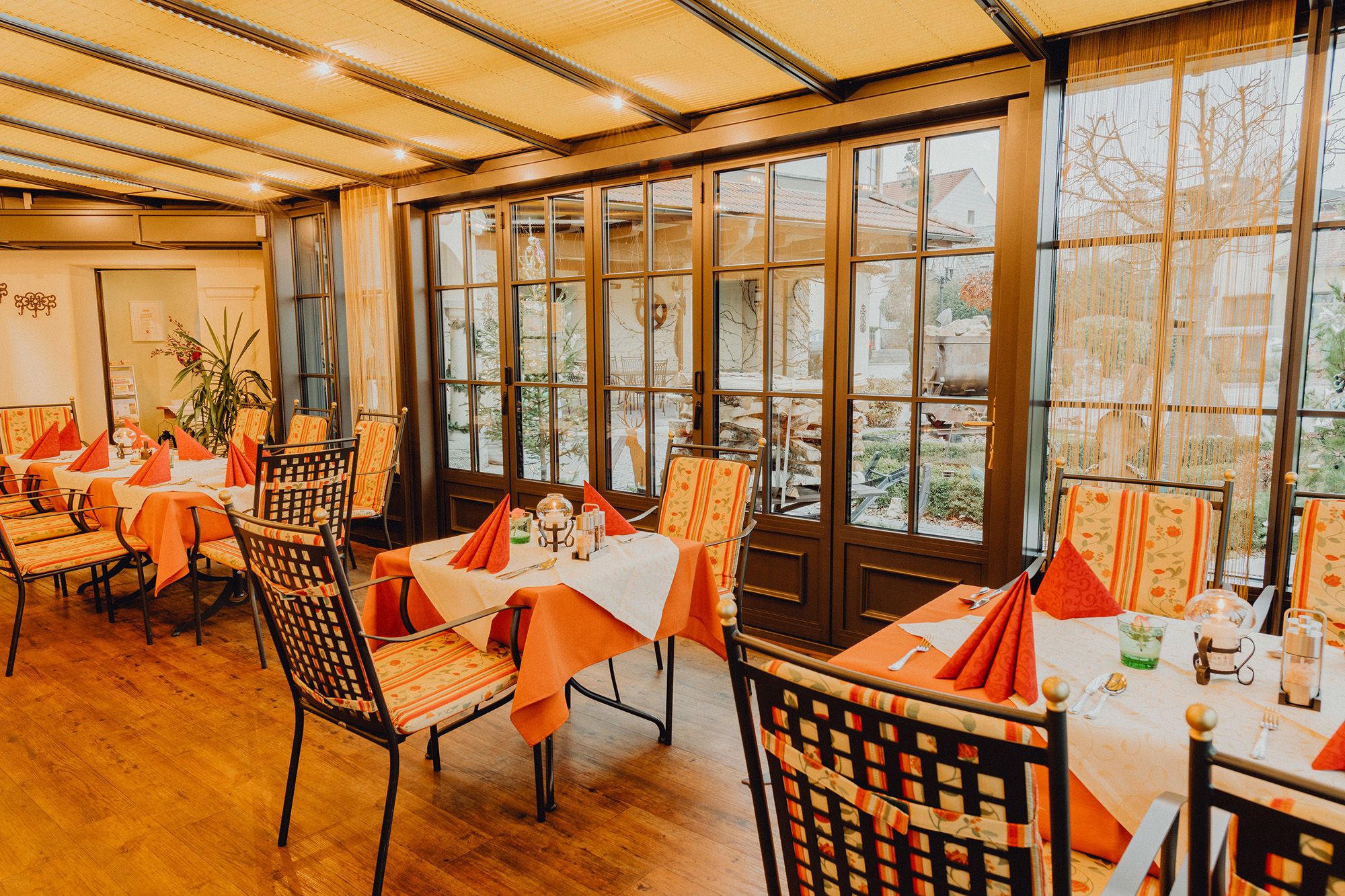 Hangulatos télikert asztalokkal és székekkel, nagy ablakokkal körülvéve, kilátással a szabadba.