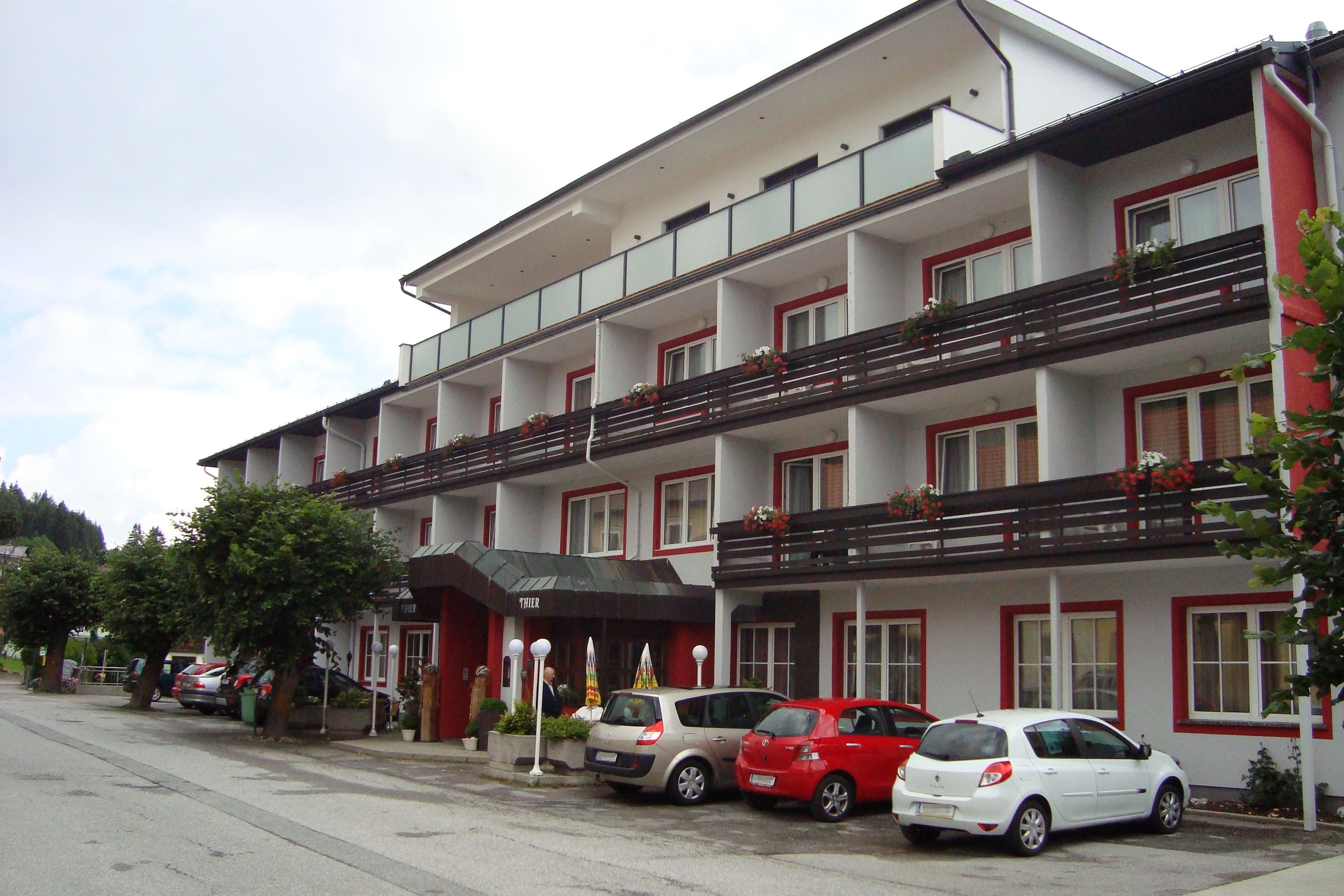 A Hotel Thier külső nézete parkoló autókkal és virágos erkélyekkel.