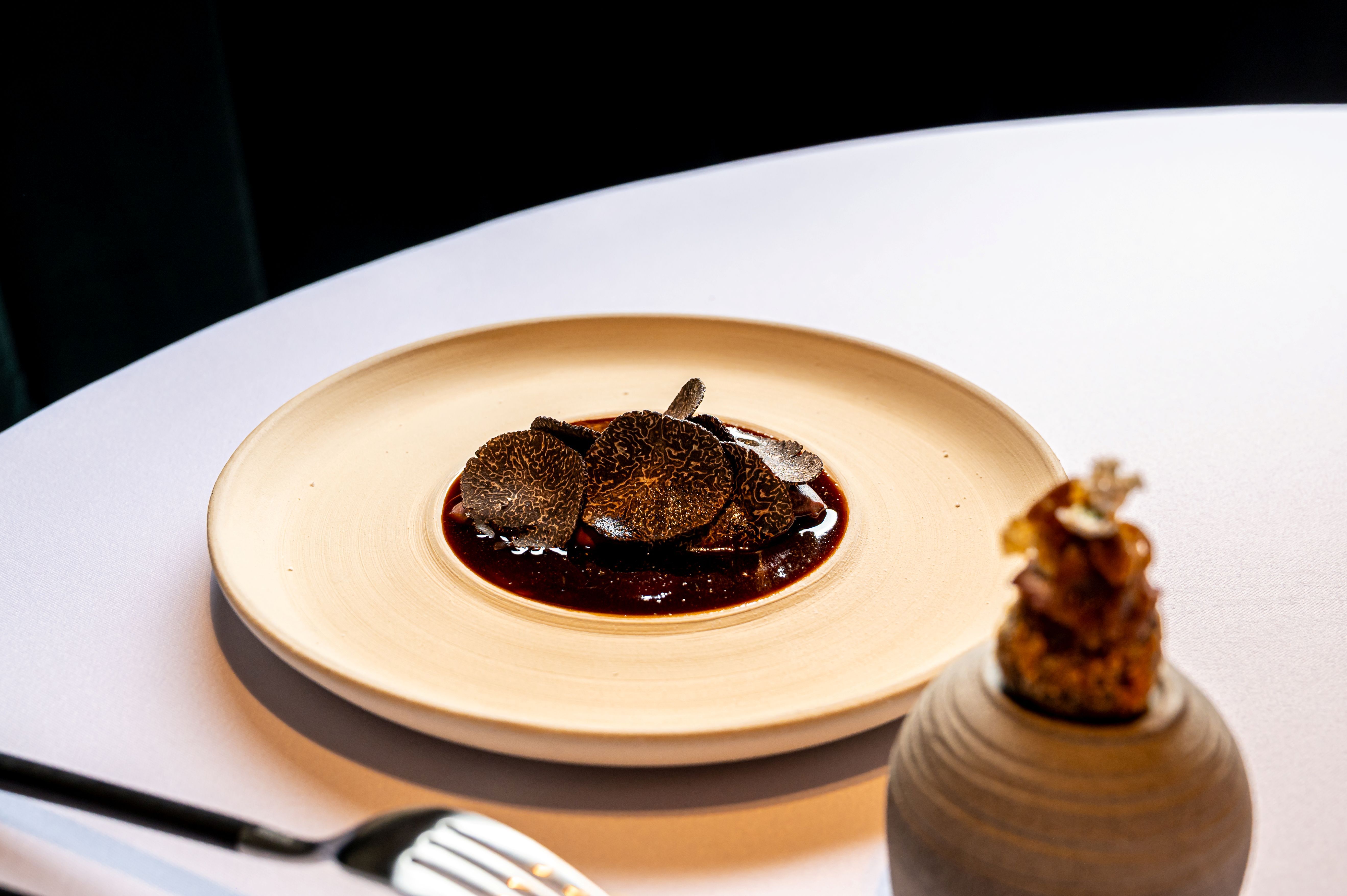 Ínyenc tál szarvasgombaszeletekkel egy tányéron, mellette egy díszítőelemmel.