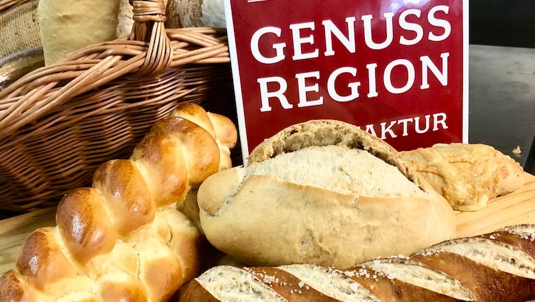 Különböző kenyérfajták a "Genuss Régiók" feliratú tábla előtt.