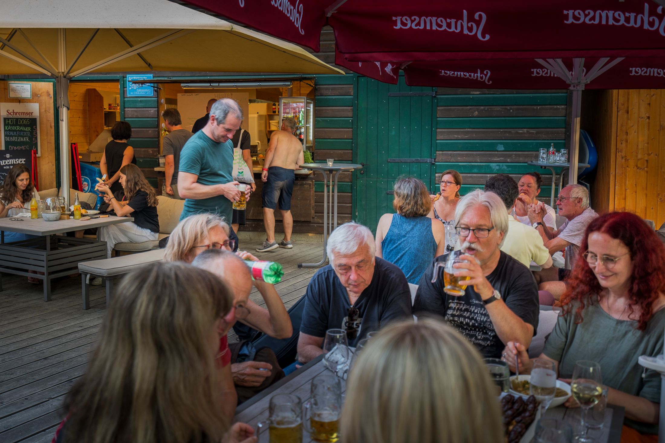 Az emberek egy sörkertben az asztaloknál ülnek, és italokat és harapnivalókat fogyasztanak.
